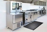 Commercial stainless steel kitchen with appliances and a black floor mat.