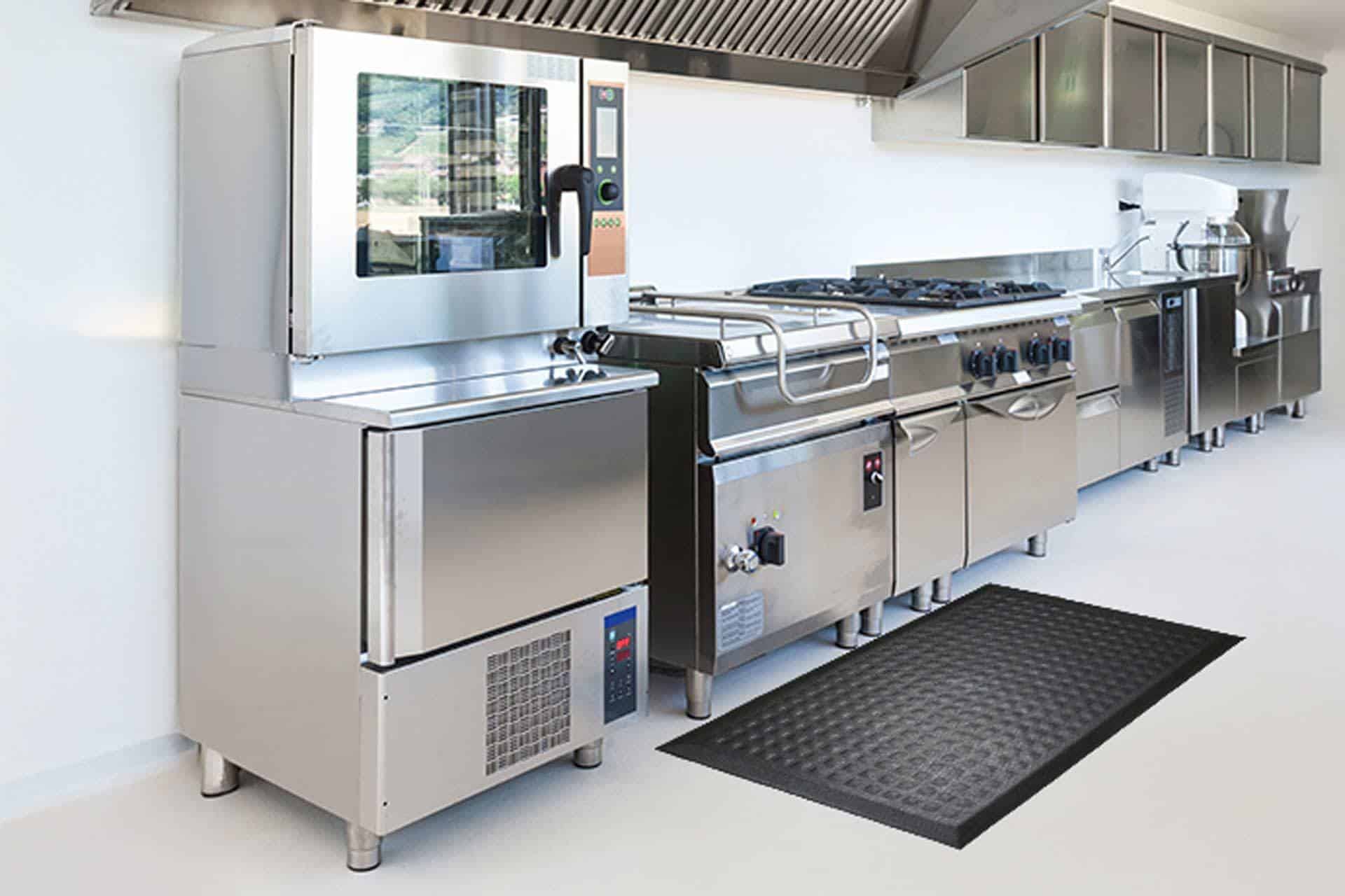 Commercial stainless steel kitchen with appliances and a black floor mat.