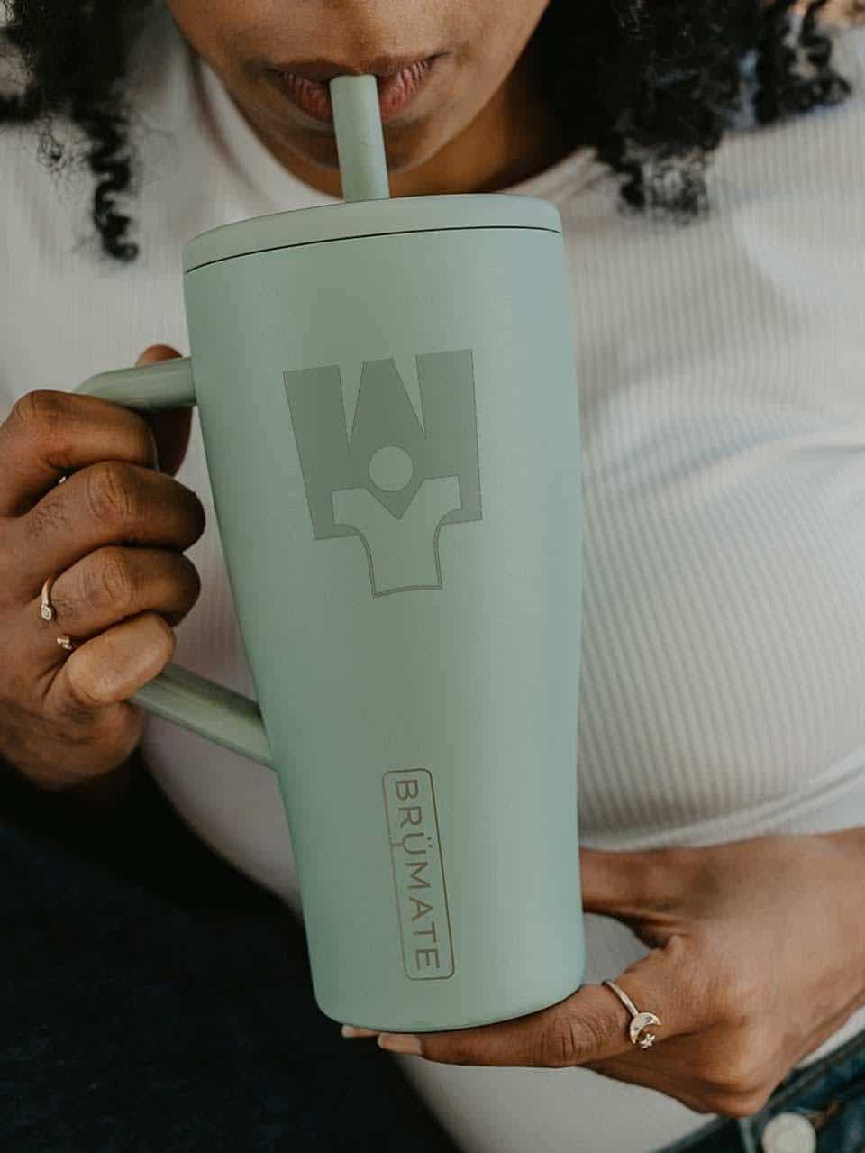 Person drinking from a large green mug with Brümate logo, sitting on couch.