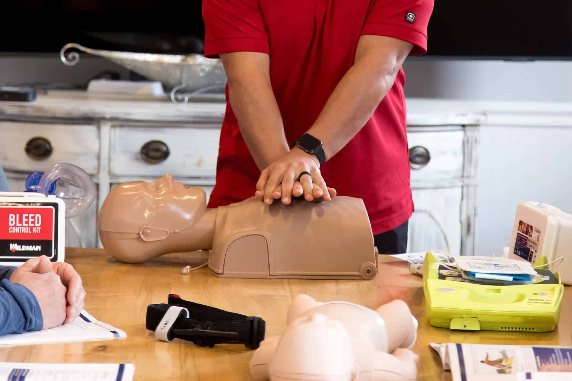 Person demonstrating CPR on a training manikin on a table.