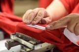 Hands placing a barcode label on red fabric using a machine.