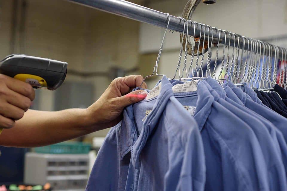 Person scanning blue shirts on hangers with a handheld device.
