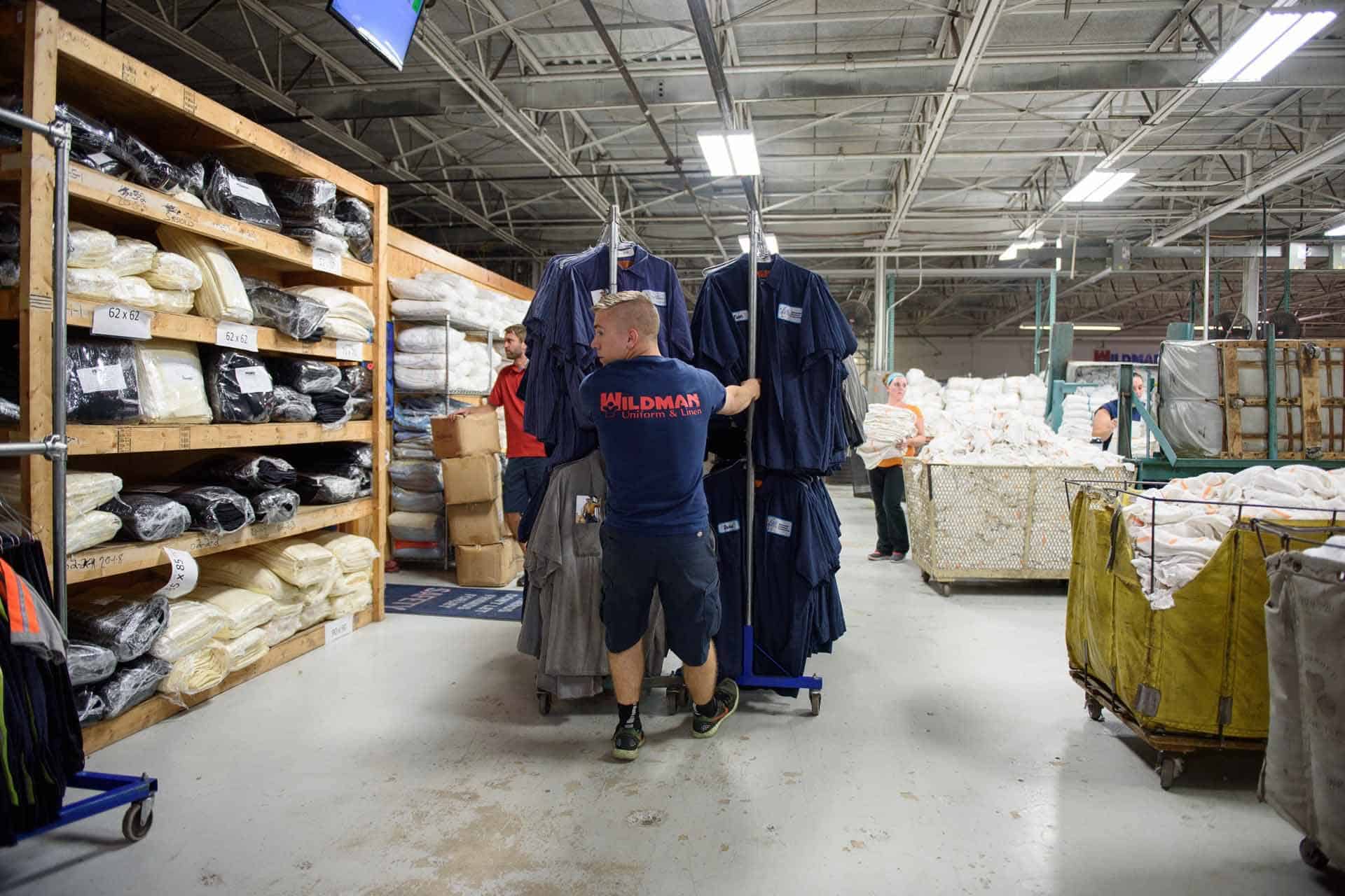 Worker managing uniforms in an organized industrial warehouse environment.