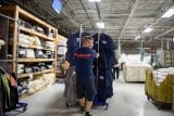 Worker organizing uniforms on racks in an industrial warehouse setting.