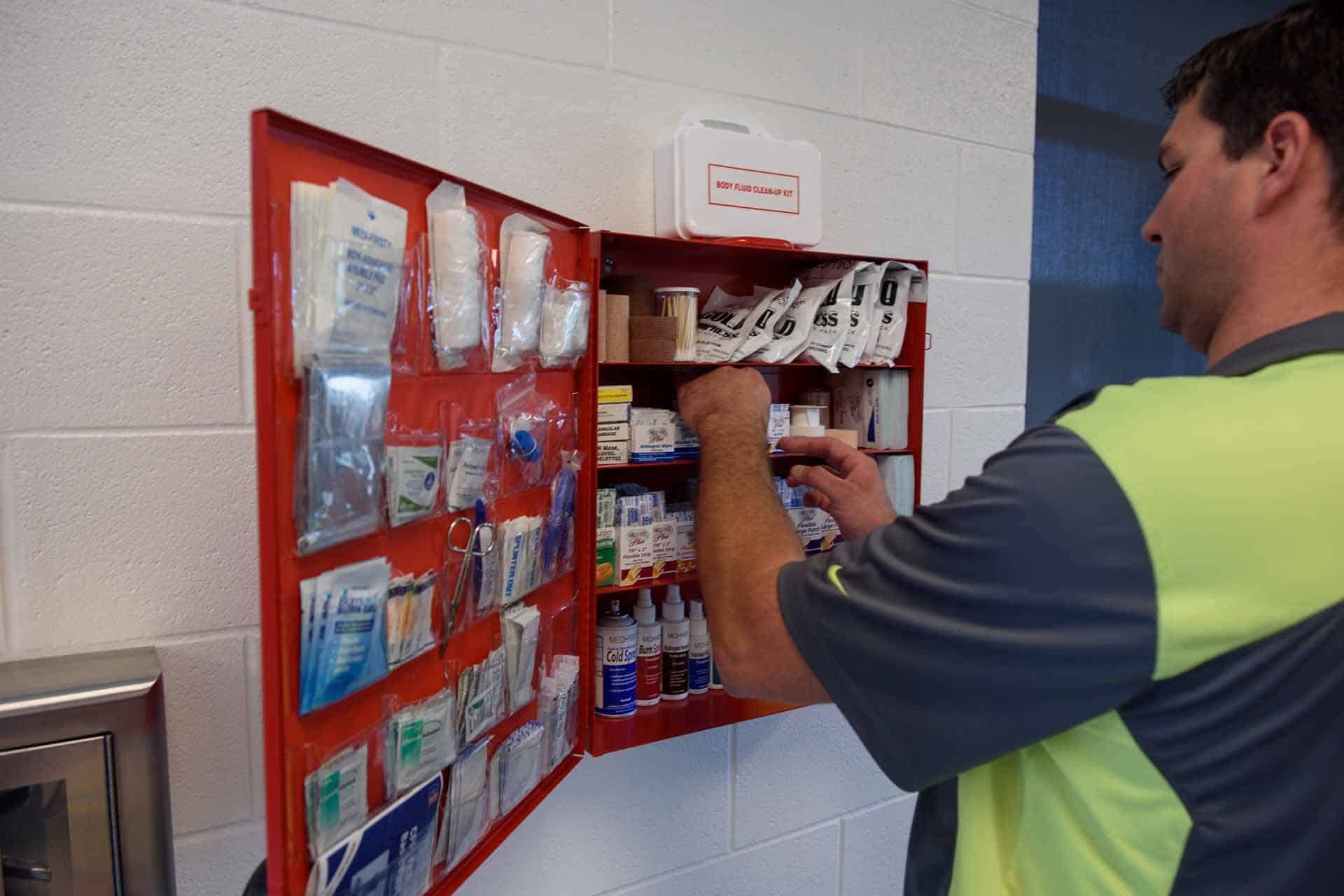 Person organizing a red first aid kit, ensuring safety on the wall.