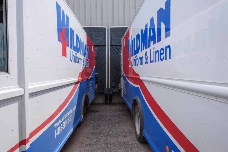 Two delivery trucks of Wildman Uniform & Linen parked close together.