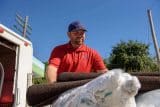 Man in a red shirt and cap unloading rolled carpets from a truck.