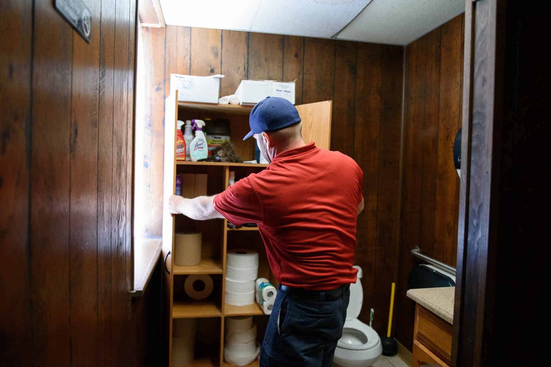 Person organizing a storage cabinet in a small restroom.