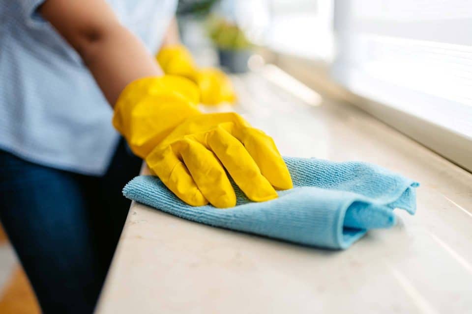 Person cleaning surface with blue cloth and wearing yellow gloves.