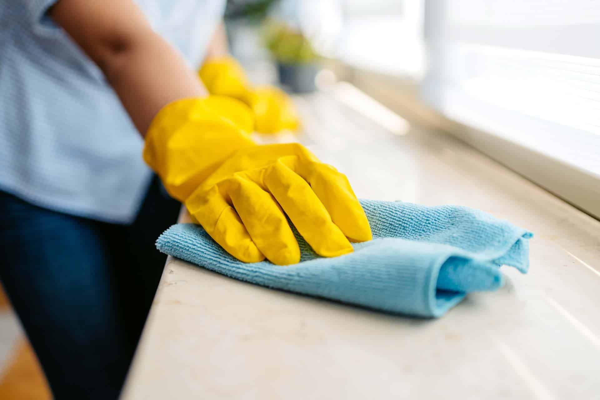 Person cleaning surface with blue cloth and wearing yellow gloves.