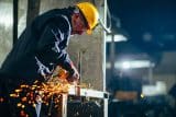 Worker in a hard hat using an angle grinder, creating sparks indoors.