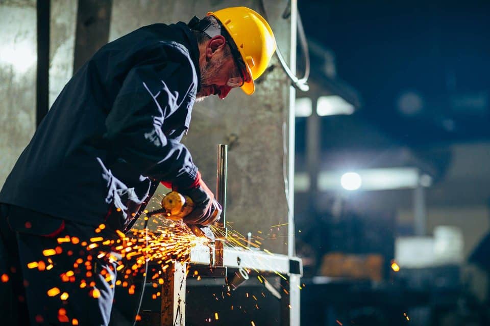 Worker in a hard hat using an angle grinder, creating sparks indoors.