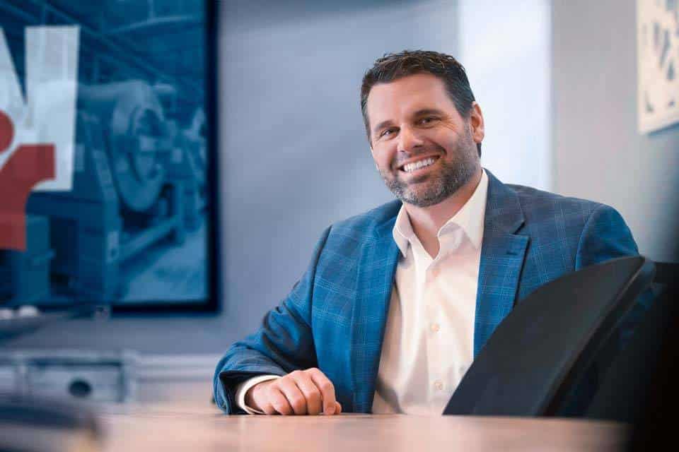 Man in a blue suit jacket smiling while seated at a conference table.