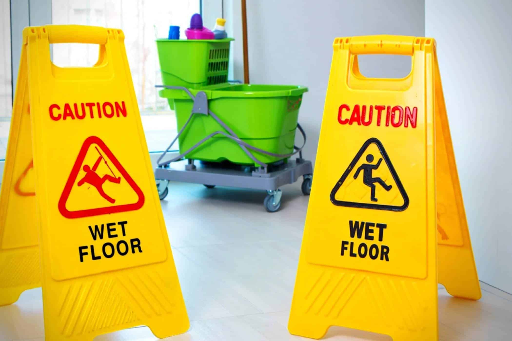 Two yellow Caution Wet Floor signs beside a cart with professional mops and bucket.