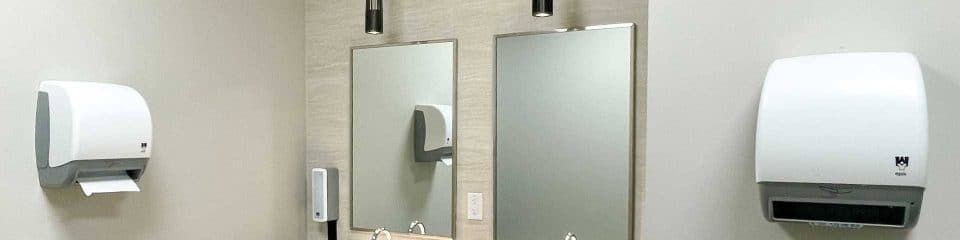 Two sinks with mirrors and wall-mounted paper towel dispensers in a restroom.