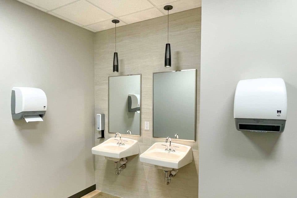 Two sinks with mirrors and wall-mounted paper towel dispensers in a restroom.