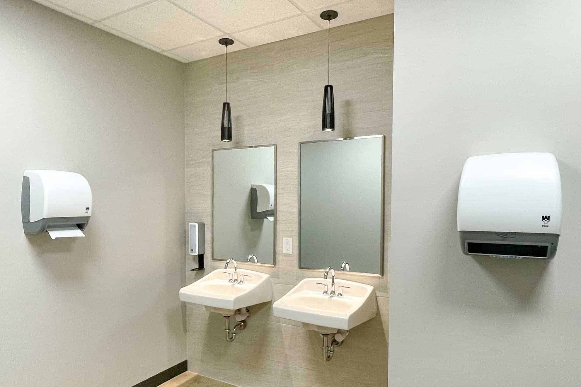 Two sinks with mirrors and wall-mounted paper towel dispensers in a restroom.