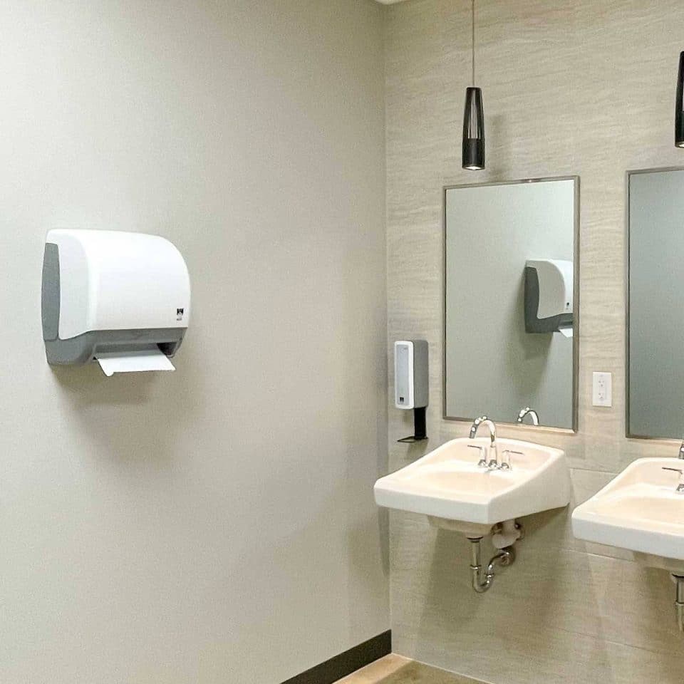 Two sinks with mirrors and a paper towel dispenser in a restroom.