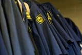 Row of blue uniforms with yellow patches hanging on a rack.