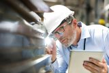 Man in hard hat inspects metal surface for OSHA inspection preparation.
