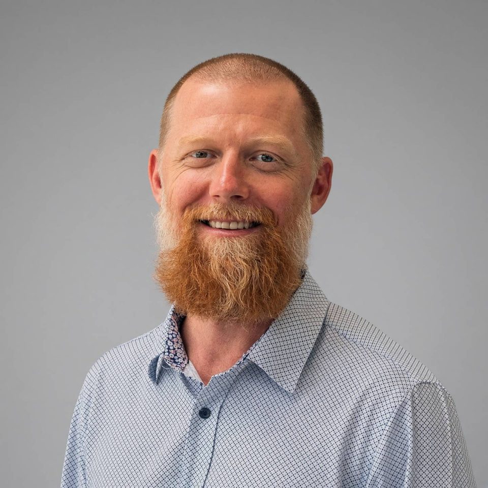 A man with a red beard wearing a patterned collared shirt.