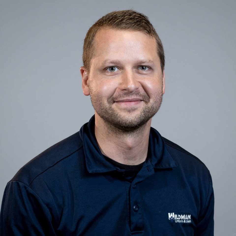 A man in a navy polo shirt with the Wildman Uniform & Linen logo.