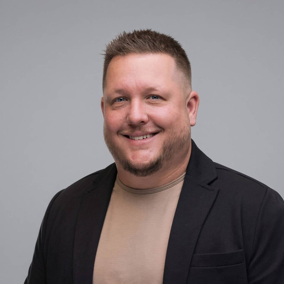 A man with a goatee wearing a tan shirt and a black blazer.