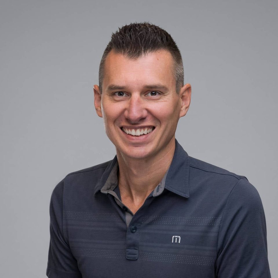 A smiling man in a dark grey polo shirt.