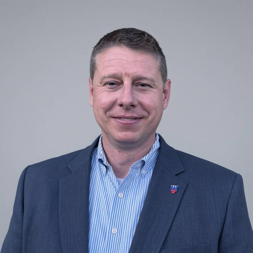Headshot of a man in a blue blazer and striped button-down shirt.