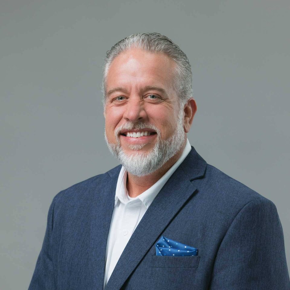 A smiling man with a grey beard wearing a blue suit jacket and pocket square.